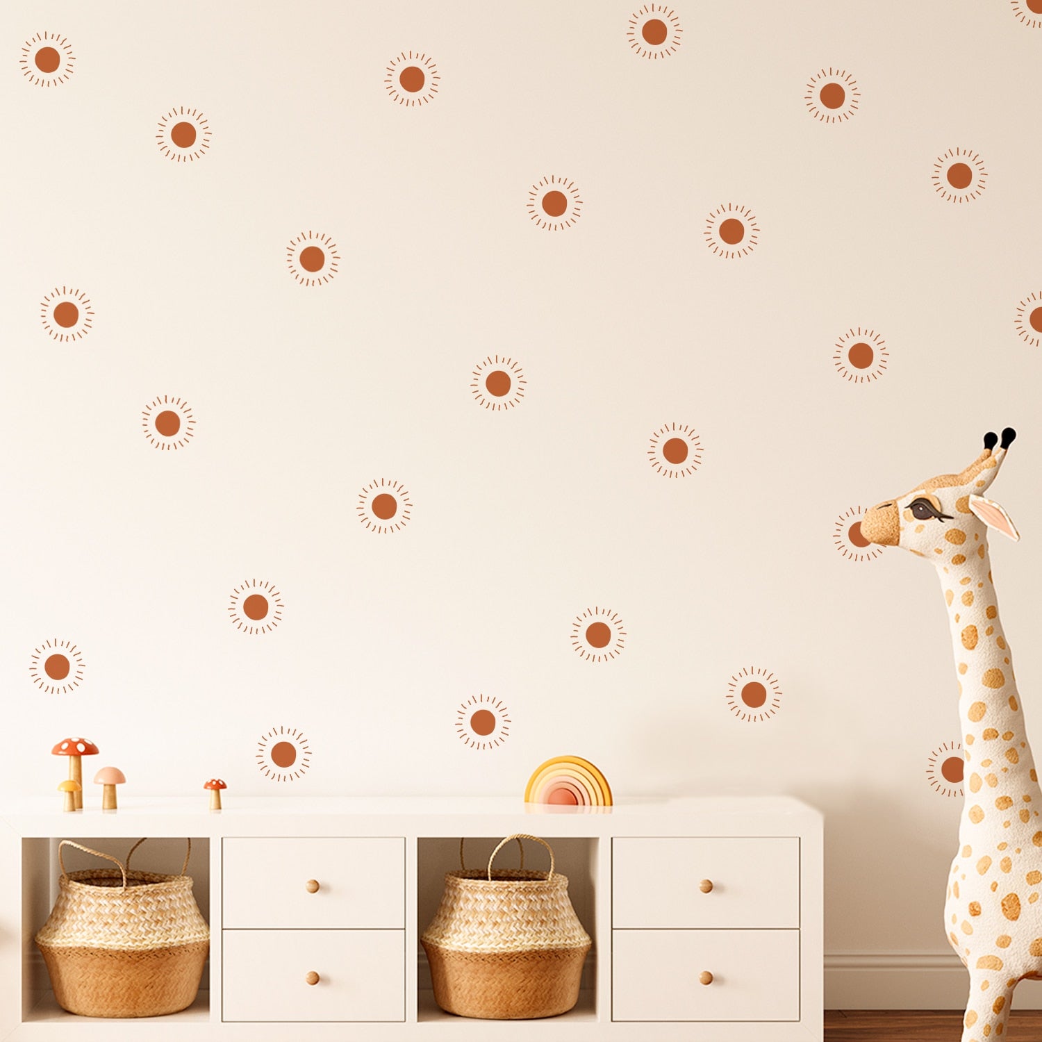 White wall with maroon sun shapes on it. Two baskets are stored inside a white console. Plush giraffe appear in the right of the photo.